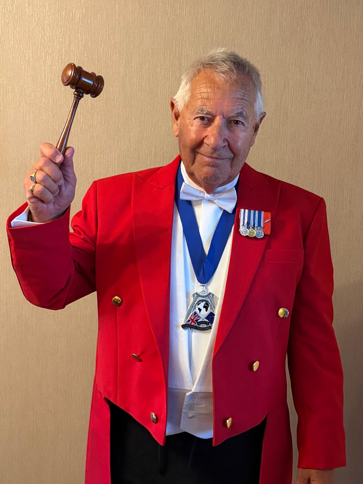 Martin Day, professional Toastmaster in a red tailcoat raising a gavel